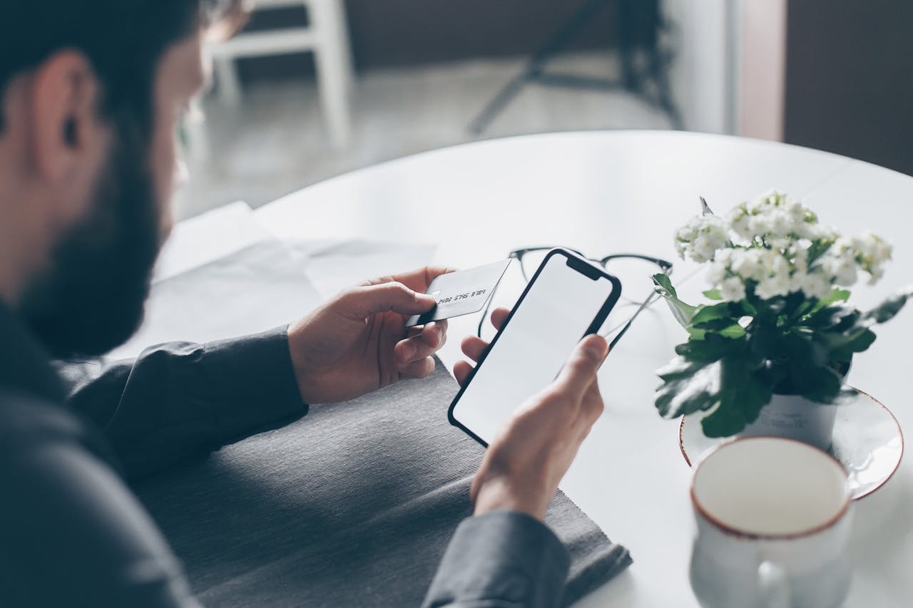 Services A man holding a credit card and smartphone at a table, engaging in online payment indoors.
